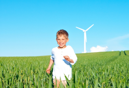 Happy child running through a green field with a wind turbine in the background, symbolizing renewable energy and a sustainable future.