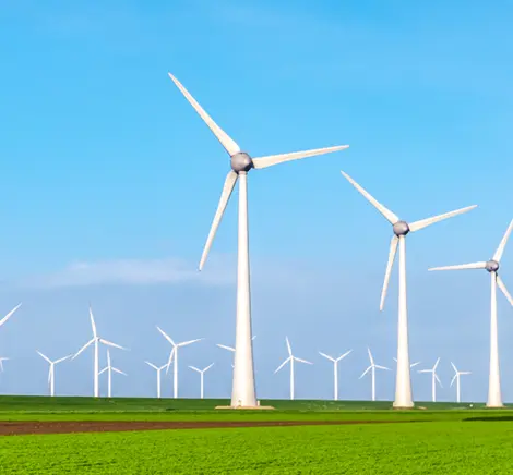 A row of wind turbines in a green field under a clear blue sky.